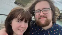 امیلیا اور لیوس ریلف مسکرا رہے ہیں۔ ان کے عقب میں سمندر کا پانی دیکھا جا سکتا ہے