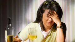 मदिराको बोतल र ग्लास अगाडि राखेर पुर्पुरोमा हात समातेर बसेकी एक महिला