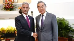 Indian foreign minister S Jaishankar on the left wearing a black suit and magenta tie as he shakes hands with Wang Yi in a grey suit and purple tie on the right
