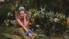 Chloe sentada em um jardim e sorrindo em direção à câmera