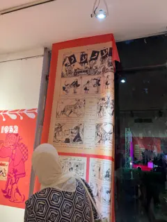 سيدة تنظر إلى لوحة من الكوميكس معلّقة على الحائط.