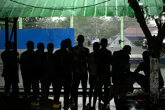 በታይላንድ መጠለያ ክፍል ጨለማ ውስጥ ተደርድርው ወደ ውጭ እያዩ የቆሙ ወንዶች