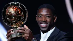 Мужчина держит в руках золотой мяч и улыбается в камеру