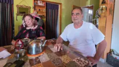 Una mujer y un hombre sentados a la mesa tomando mate