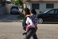 Deysi Vargas carrega nas costas sua filha Sofia pela rua