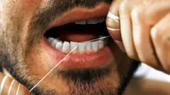 Imagem da boca e do rosto de um homem passando fio dental entre os incisivos