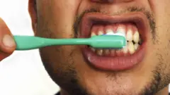 Close-up seorang pria muda sedang menyikat gigi. Menyikat gigi secara teratur membantu mencegah kerusakan gigi dan penyakit gusi.