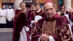 Fotografia colorida mostra cena do filme com Ralph Fiennes, um homem branco, ficando calvo, com roupas e paramentaçãosport recife xcardeal 