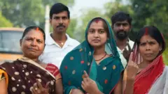 ভোটদানের পর আঙুল তুলে অমোচনীয় কালি দেখাচ্ছেন শাড়ি পরা তিন জন নারী, তাদের পেছনে দুই জন পুরুষ।