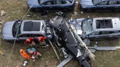 Imagem aérea de helicóptero caído em cima de carros.