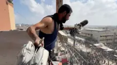 Эркек киши Насер ооруканасынан түз эфирге чыккан журналист Хусам аль-Масринин жабдыктарын кармап турат