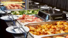 Bandejas de desayuno buffet con papas al horno, tocino, brócoli, huevos y otros platillos.