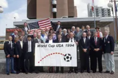 Grupo de pessoas perfiladas exibe a bandeira da Copa do Mundo de 1994