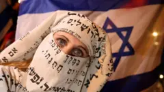 İbranice harflerden burka yapan bir Yahudi kadın İsrail bayrağı önünde duruyor. Yalnızca gözleri var.