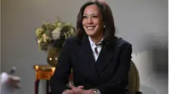 Kamala Harris, Igbakeji aarẹ America tẹlẹ lo n rẹrin ẹyẹ yii. O da irun rẹ walẹ, o si wọ aṣọ oyinbo ti awọ rẹ dudu, pẹlu funfun ninu rẹ.