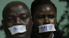 Duas pessoas negras com um esparadrapo na boca protestando por mais financiamento