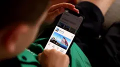 طفل يرتدي تيشيرتا أخضر وشورتا أسود، ينظر إلى أحد الألعاب على منصة روبلوكس من خلال هاتف محمول.