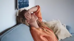 Uma mulher deitada em uma poltrona com uma das mãos na cabeça.
