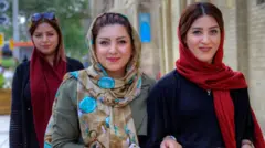 Jovens mulheres iranianas, vestidas com hijab, caminham por uma rua.