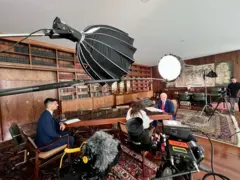 Equipamentos de filmagem em sala; Lula está sentando diante de dois repórteres da BBC