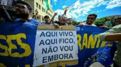 Pessoas se manifestando e segurando um cartaz escrito "Aqui vivo, aqui fico, não vou embora"