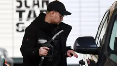 Umugabo wambaye ingofero y’umukara n’ikoti arimo kongera amavuta mu imodoka ye kuri sitasiyo ya peteroli i Londres, ku wa 29 Werurwe 2026.