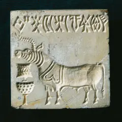 Uma placa de pedra quadrada entalhada, com a figura de um animal de perfil e uma fileira de símbolos na parte superior. A superfície da pedra apresenta rachaduras e desgaste