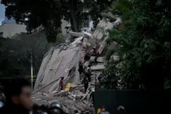 La fachada de un edificio colapsado mientras rescatistas escalan el muro en búsqueda de víctimas