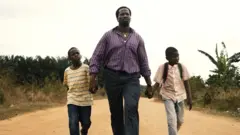 Homem caminhando em rua de terra de mãos dadas com os dois filhos