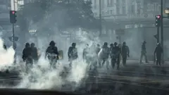 Полицейские в защитной форме в Париже переходят улицу в дыму от горящих мусорных баков