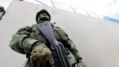 Un soldado con la cara cubierta y casco sostiene un fusil.