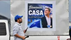 Un hombre pasa frente a una pancarta de bienvenida al expresidente Hernández.