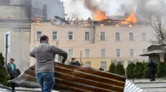 A man clears debris as a building burns in the background after Russian strikes on Lviv on Tuesday