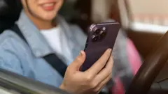 A close-up of a positive Asian woman using her smartphone while stopped at traffic in the city. 