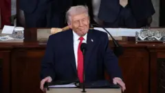 Donald Trump kürsüde, keyifli bir şekilde gülüyor.