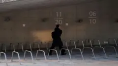 黒い上着に黒いズボン、黒いバックパックを身に着けた女性が、右手で携帯電話を持ち、話しながら歩いている