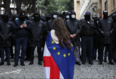 A young woman draped in Georgian and EU flags stands in front of a line of riot police