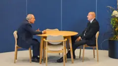 Qeyri formal görüşdə Nikol Paşinyan masa arxasında qarşıda oturan İlham Əliyevə doğru nisbətən əyilərək nəsə danışır, Əliyev isə müvazinətini pozmadan, stolun altında əlləri bir-birinə keçmiş vəziyyədə onu dinləyir.