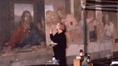 Brambilla em frente ao mural com um pincel na mão