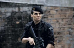 Wagner Moura aparece como capitão Nascimento em cena do filme Tropa de Elite, vestindo uniforme preto do Bope, o Batalhão de Operações Policiais Especiais. Ele segura um fuzil enquanto observa o entorno com expressão tensa.