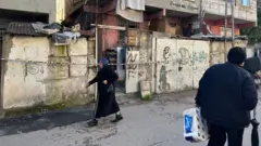 Yangının yaşandığı binanın girişi ve sokakta yürüyen iki kişi 