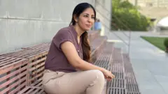 Mulher sentada na escada em ambiente externo, olhando para longe da câmera