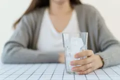 Mujer con un vaso lleno de hielo en primer plano