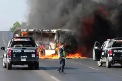 Caminhonetes da polícia municipal ao lado de um ônibus incendiado por grupos criminosos após operação em Jalisco, em Zapopan, em 22/2/2026
