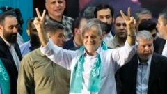 İran prezidenti Məsud Pezeşkian kütlənin önündə dayanaraq gülümsəyir. Onun boynunda yaşıl şərf var. 