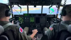 Cabine de comando de avião se preparando para pousar nas ilhas Marshall, com o comandante do 53° Esquadrão de Reconhecimento Climático, coronel Stephen Pituch, e o capitão Nate Wordal