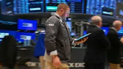 Um operador passa segurando um tablet no pregão da Bolsa de Valores de Nova York, na abertura do pregão de 21 de abril de 2025. Atrás dele, telas azuis desfocadas mostram os mercados