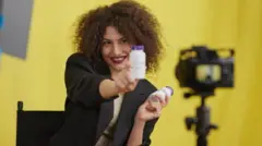 Mulher em frente a uma câmera promove produtos em frascos em suas mãos