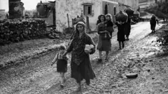 Mulheres carregando seus filhos por uma rua de terra