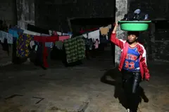 سيدة من أثيوبيا في مرآب تحمل سلة ملابس وخلفها ثياب معلقة على حبل غسيل